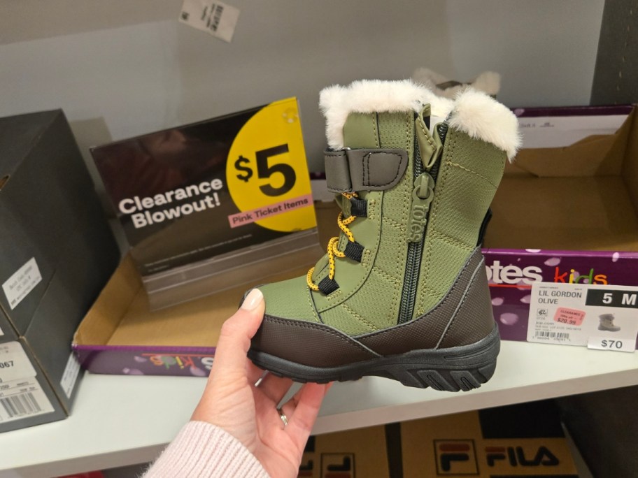hand holding a kids winter boot in front of a clearance sign on a store shelf