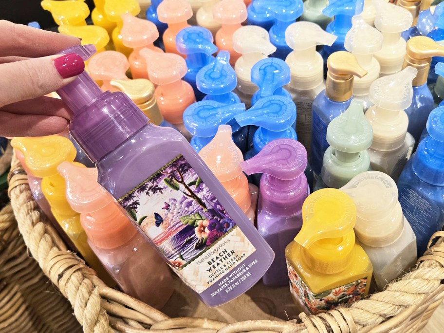 hand grabbing a purple Bath & Body Works Hand Soaps from a basket with a variety of scents