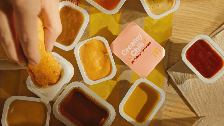 various cups of mcdonalds dipping sauces on a table, most open, one creamy chili one still sealed